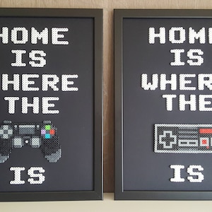 May include: Two framed black and white pixel art prints with the text "Home is where the ___ is" with a video game controller in the first frame and a NES controller in the second frame.