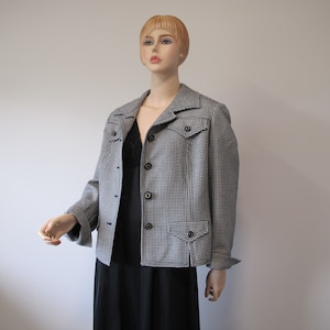 Könnte beinhalten: Eine Jacke im schwarz-weißen Hahnentrittmuster mit Knopfleiste und Pattentaschen.
