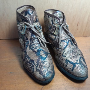 May include: A pair of brown and blue snakeskin ankle boots with gold buckles and laces.