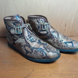 May include: A pair of brown and black snakeskin ankle boots with gold buckles. The boots have a lace-up front and a rounded toe.