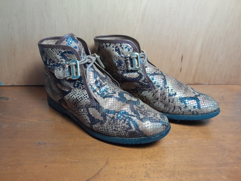 May include: A pair of brown and black snakeskin ankle boots with gold buckles. The boots have a lace-up front and a rounded toe.