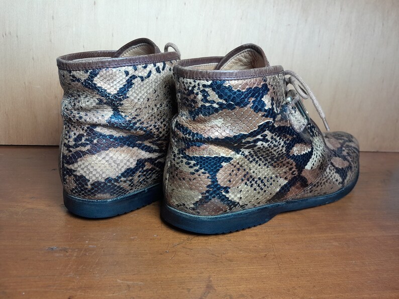 May include: A pair of brown and black snakeskin ankle boots with laces. The boots have a rounded toe and a flat sole.