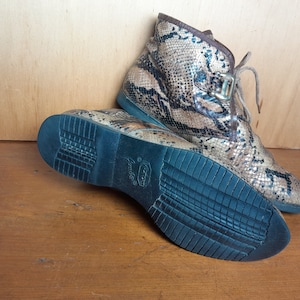 May include: A pair of brown and black snakeskin ankle boots with a black rubber sole. The boots have a lace-up closure and a buckle detail.