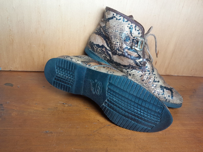 May include: A pair of brown and black snakeskin ankle boots with a black rubber sole. The boots have a lace-up closure and a buckle detail.