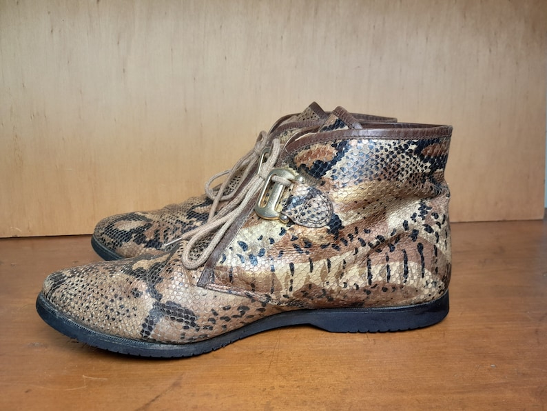 May include: Brown and gold snakeskin ankle boots with a buckle fastening. The boots have a lace-up front and a chunky heel.