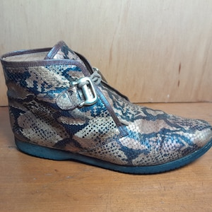 May include: Brown ankle boots with a snakeskin pattern and a gold buckle. The boots have a lace-up closure and a rounded toe.