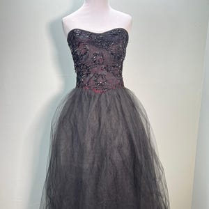 May include: A strapless formal dress with a black tulle skirt and a beaded bodice. The bodice is embellished with sequins and beads, and the skirt is layered. The dress is displayed on a mannequin.