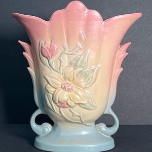 May include: A vintage ceramic vase with a pink and blue glaze. The vase features a raised floral design with a large magnolia flower and leaves.