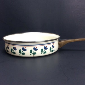 May include: White enamel saucepan with a blue and green floral pattern around the rim and a wooden handle.