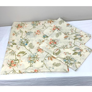 Puede incluir: Juego de cama floral color crema con una colcha grande y dos fundas de almohada. El diseño incluye ramas con flores coloridas en tonos naranja, azul y verde. La ropa de cama está hecha de una tela suave y ligera.