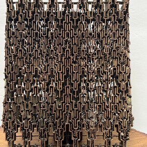 May include: A close-up of a copper-coloured metal object with a complex, geometric pattern. The object is made up of many small, interconnected pieces, creating an intricate design. The object appears to be a vintage or antique piece.