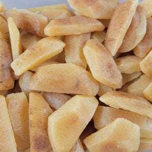 May include: Close-up of a pile of frozen potato wedges. The wedges are a light yellow color with some brown spots, and they are cut into various shapes and sizes. The image is well-lit and shows the texture of the food.