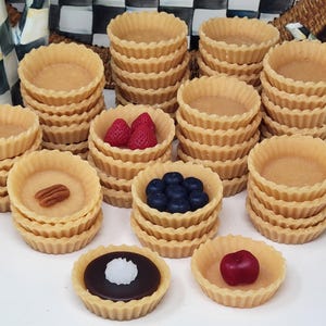 May include: Stacks of empty, fluted tart shells, some filled with fresh fruit and a pecan. The fruit includes strawberries, blueberries, and a cherry. The tarts are arranged on a white surface, suggesting a dessert theme.