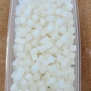 May include: A clear plastic container filled with small, white, cube-shaped pieces of soap.