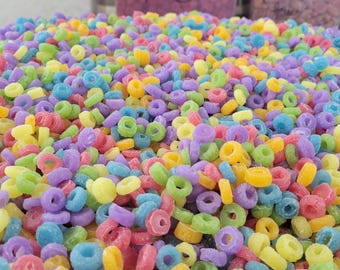 May include: A close-up of a large pile of colorful cereal rings. The rings are in shades of pink, purple, yellow, and blue.
