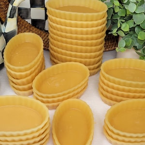 May include: A collection of pre-baked, oval-shaped tart shells with a fluted edge, filled with a golden-yellow custard. Several stacks and individual shells are arranged, suggesting a baking or dessert theme. The background includes decorative elements.