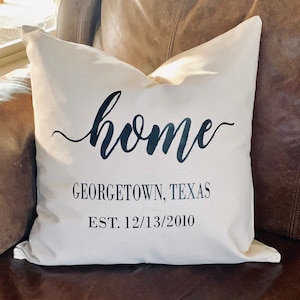 May include: White throw pillow with black text that reads "home" in cursive, "GEORGETOWN, TEXAS" and "EST. 12/13/2010".