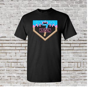 May include: Black t-shirt with a baseball diamond graphic. The diamond is filled with blue and pink frosting with sprinkles. The number 7 is in the center of the diamond with the name "KAISON" below it.