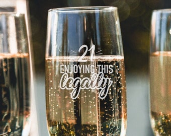 May include: Three champagne flutes filled with sparkling wine. The center flute has the text "21 ENJOYING THIS LEGALLY" etched on the side.