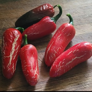 May include: Six red jalapeño peppers on a wooden chopping board. The peppers have a white stripe pattern and are ready to be used in cooking.