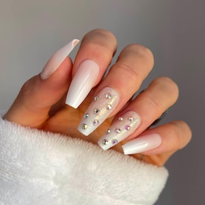 May include: White ombre press-on nails with a glitter finish and iridescent rhinestones.