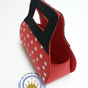 May include: Red handbag with white polka dots and a black handle. The bag has a rectangular opening and a curved body. The logo "Royal Baby Baby Us" is visible on the bottom.