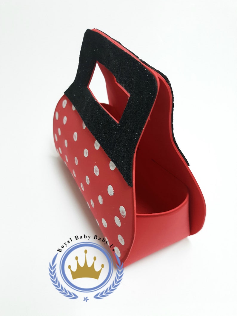 May include: Red handbag with white polka dots and a black handle. The bag has a rectangular opening and a curved body. The logo "Royal Baby Baby Us" is visible on the bottom.