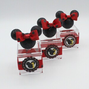 K&ouml;nnte beinhalten: Drei transparente Acrylboxen mit schwarzen und roten Minnie Mouse Ohren und Schleifen. Jede Box hat ein schwarz-rotes gepunktetes Band und einen schwarzen und gelben Kreis mit einem Minnie Mouse Kopf und der Nummer 1, 2 oder 3.