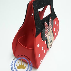 May include: Red Minnie Mouse-themed handbag with white polka dots and a black glitter handle. The bag features a Minnie Mouse face and bow. The bag has a compartment inside and is designed for carrying small items.