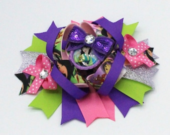 May include: A decorative hair bow featuring a central image of a cartoon character, surrounded by layers of purple, pink, green, and silver ribbons. The bow includes sequined accents and rhinestone embellishments, creating a layered and colorful design.