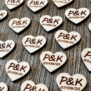 May include: A collection of wooden heart-shaped wedding favors with the initials "P&K" and the date "07/09/25" engraved on each.