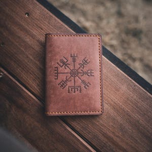 May include: A brown leather wallet with a compass design embossed on the front.