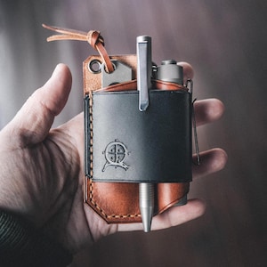 May include: A brown leather pocket organizer with a black leather insert. The organizer has a pen holder, a small pocket for a knife, and a compass logo on the front.