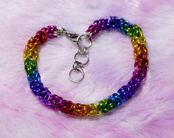 May include: A rainbow-colored chainmail bracelet with a silver clasp and adjustable chain. The bracelet features a gradient of colors, including red, orange, yellow, green, blue, and purple. The bracelet is made of small, interlocking metal rings.