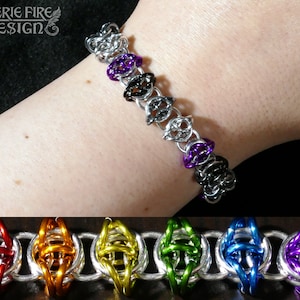 May include: A silver chain bracelet with colourful, woven, metal rings. The rings are in the colours red, orange, yellow, green, blue, and purple.