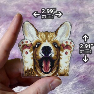May include: A clear sticker with a pixelated image of a corgi dog with its paws up, looking at the camera with its tongue sticking out. The sticker is 2.99 inches wide and 2.91 inches tall. The sticker has the text "PIKIR 2021" in the bottom left corner.