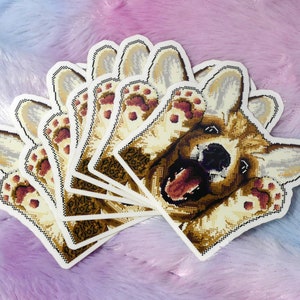 May include: A set of eight stickers featuring a cartoon corgi dog with its paws up in the air. The dog has a brown and white coat and is smiling with its tongue sticking out. The stickers are printed on white paper and have a glossy finish.