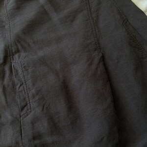 May include: A dark charcoal gray garment featuring vertical seam detailing and two visible side pockets. The fabric has a subtle, slightly textured weave with visible stitching along the pocket openings and the vertical panel seams.