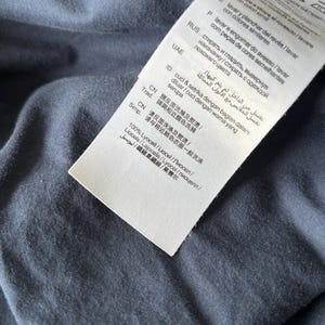 Puede incluir: Primer plano de una tela azul marino con una etiqueta blanca adjunta. La etiqueta contiene instrucciones de lavado en varios idiomas, incluido el espa&ntilde;ol. La tela parece suave y ligeramente texturizada.
