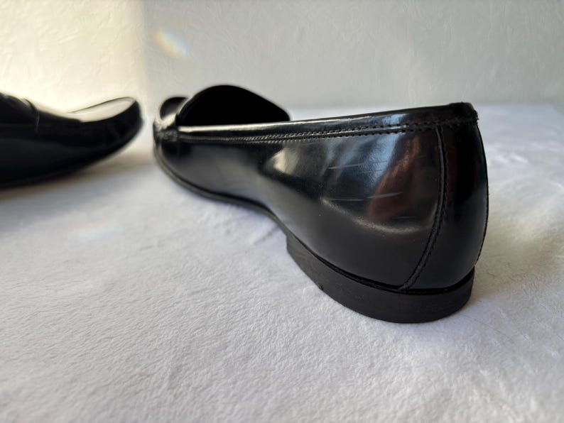 Może przedstawiać: Zbliżenie pary czarnych sk&oacute;rzanych mokasyn&oacute;w. Buty mają błyszczące wykończenie i klasyczny design. Obraz podkreśla elegancką sylwetkę i jakość sk&oacute;ry.