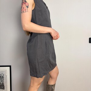 May include: A sleeveless charcoal gray dress featuring a round neckline, vertical seam detailing along the bodice, and side pockets. The dress has a straight silhouette that falls above the knee, constructed from a solid-colored fabric with visible stitching.
