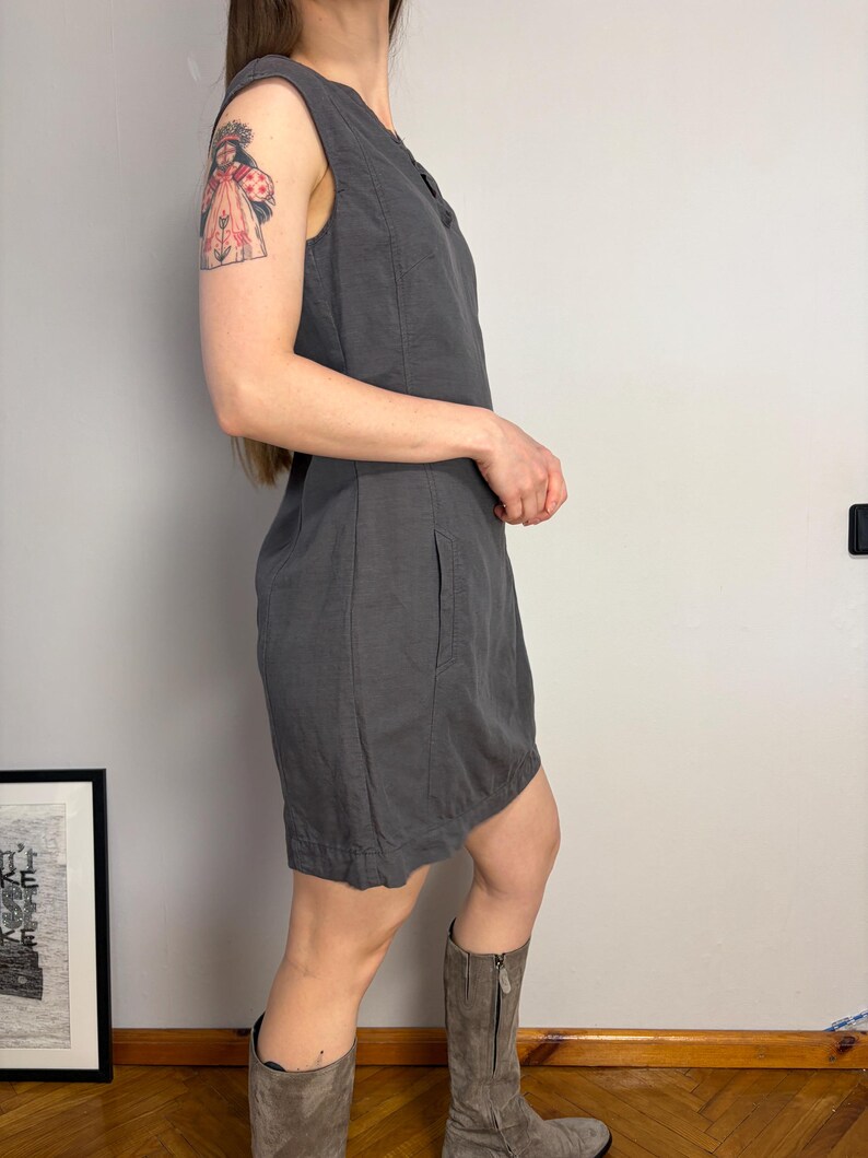 May include: A sleeveless charcoal gray dress featuring a round neckline, vertical seam detailing along the bodice, and side pockets. The dress has a straight silhouette that falls above the knee, constructed from a solid-colored fabric with visible stitching.
