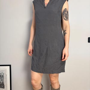 May include: A sleeveless charcoal gray knee-length dress featuring a split V-neckline, a structured bodice with a diagonal seam detail running from the shoulder to the hip, and a straight hemline. The garment has a simple, clean design.
