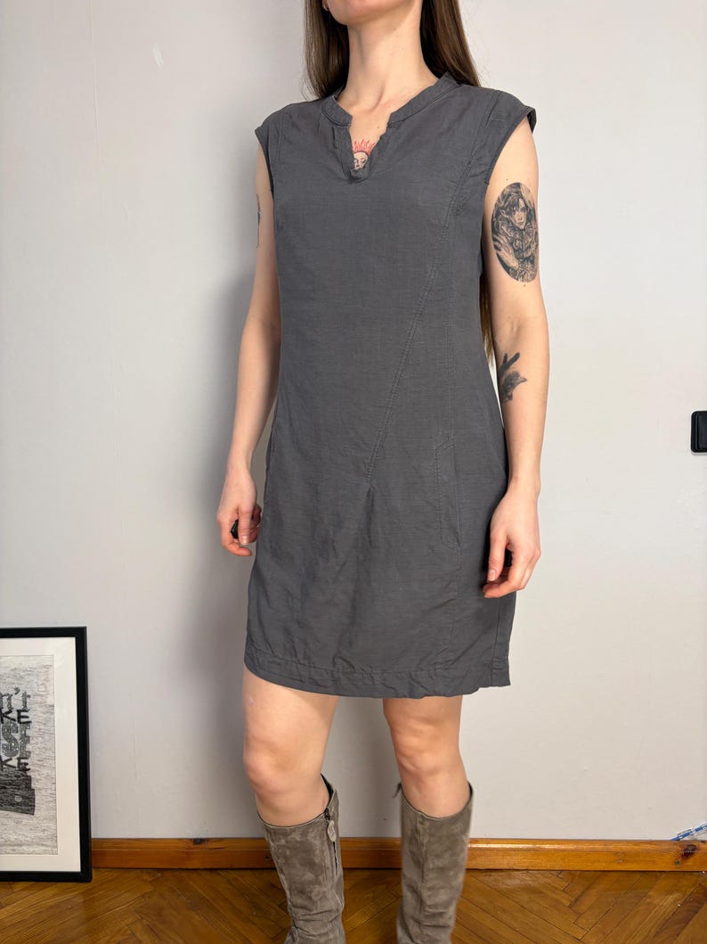 May include: A sleeveless charcoal gray knee-length dress featuring a split V-neckline, a structured bodice with a diagonal seam detail running from the shoulder to the hip, and a straight hemline. The garment has a simple, clean design.