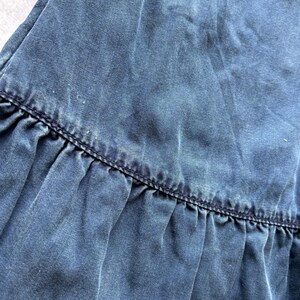 Puede incluir: Primer plano de una tela vaquera azul con un dobladillo con volantes. La tela tiene un aspecto descolorido con textura visible y sutiles variaciones de color. El dobladillo est&aacute; detallado con costuras azul oscuro.