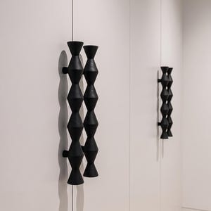 Könnte beinhalten: Schwarze, geometrische Schrankgriffe mit einem gestapelten Sanduhr-Design. Die Griffe sind an einer weißen Schranktür angebracht. Das Design wiederholt sich auf einer zweiten Schranktür im Hintergrund.
