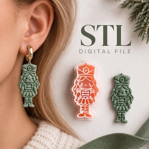 May include: A sage green nutcracker earring with a gold hoop, a matching orange nutcracker cookie cutter, and a sage green nutcracker clay piece. The text STL DIGITAL FILE is visible. The items feature a detailed soldier design with a hat and uniform.