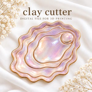 May include: A clay cutter digital file for 3D printing featuring an iridescent, wavy-edged oyster shell shape with a pearl accent. The design has a glossy, light purple and pink finish with gold-toned outlines on a white fabric background.