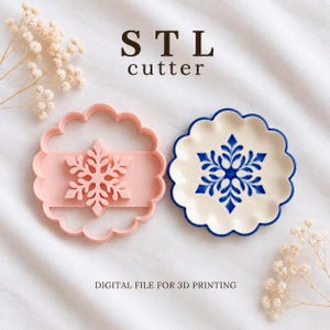 Puede incluir: Un cortador de galletas de plástico rosa claro con forma de copo de nieve y un plato redondo de cerámica con bordes festoneados y un diseño de copo de nieve azul. El texto STL cutter y DIGITAL FILE FOR 3D PRINTING se ve junto a flores blancas.