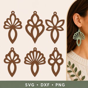 May include: A collection of six brown, laser-cut, decorative earring shapes featuring symmetrical, openwork floral and fan-like patterns. One light green version of the earring is shown hanging from an ear, displaying the cutout design.